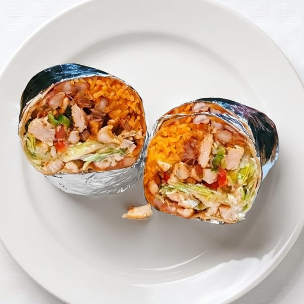 Two foil-wrapped burritos, cut in half, revealing chicken, rice, beans, and vegetables on a white plate.