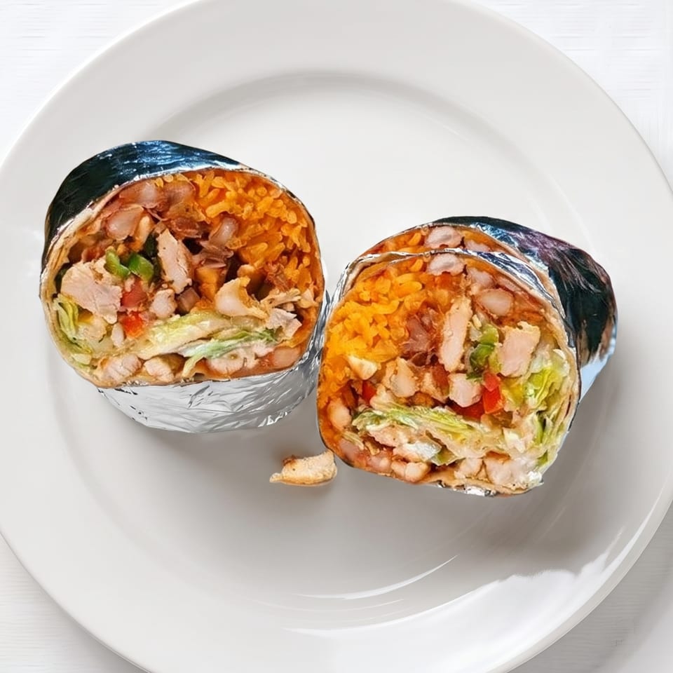 Two foil-wrapped burritos, cut in half, revealing chicken, rice, beans, and vegetables on a white plate.