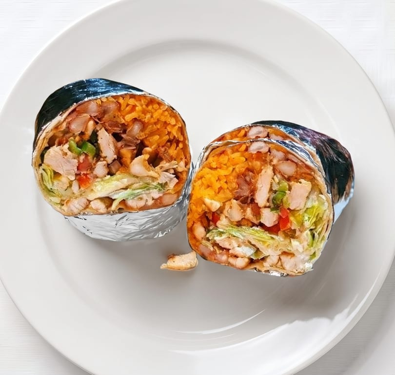 Two foil-wrapped burritos, cut in half, revealing chicken, rice, beans, and vegetables on a white plate.